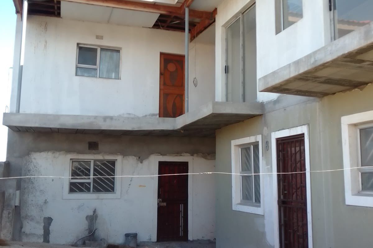 Rear view of a multi-story apartment building showing unfinished exterior plastering, exposed roof structure, and concrete balcony areas requiring completion.