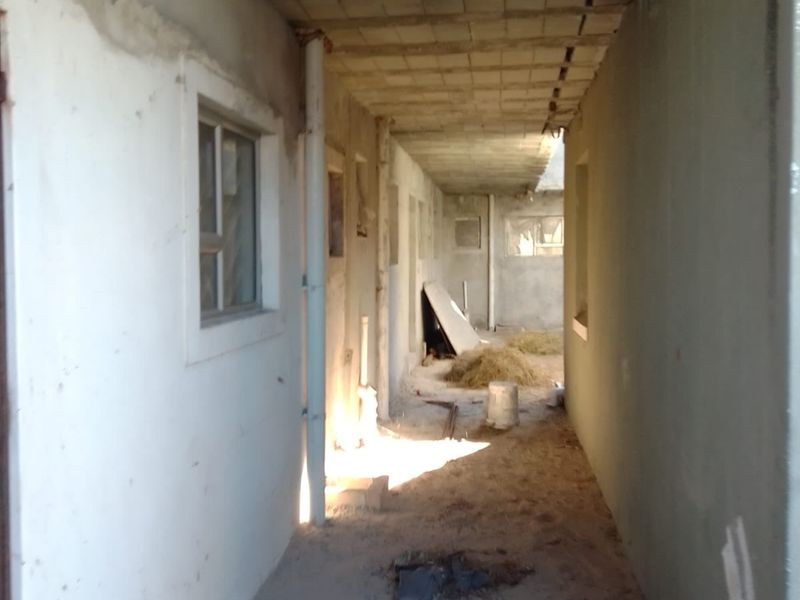 An unfinished hallway corridor in a property under construction, featuring exposed concrete ceilings, plastered walls, and basic window frames.