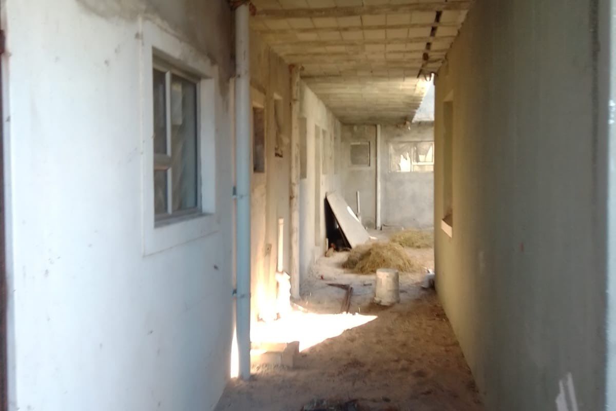 An unfinished hallway corridor in a property under construction, featuring exposed concrete ceilings, plastered walls, and basic window frames.