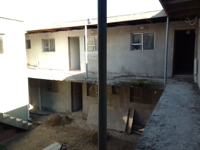 Exterior view of a multi-level apartment building under construction or renovation, featuring unfinished concrete walls, exposed rafters, and damaged window frames.