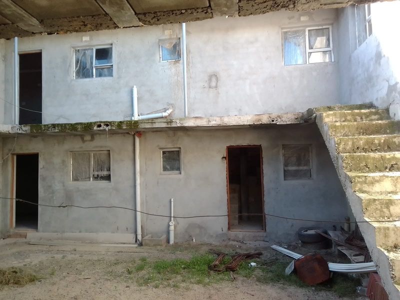 Rear view of an unfinished apartment building structure featuring exposed concrete walls, an external staircase, and basic window installations.