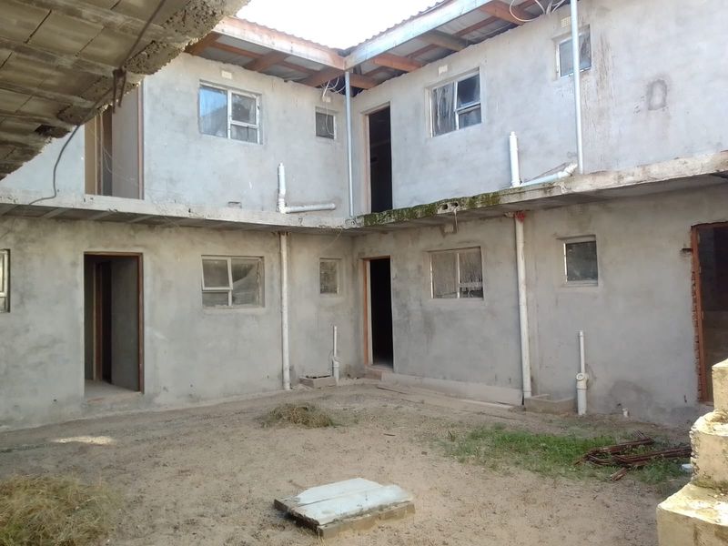 An unfinished two-story apartment building exterior featuring exposed concrete walls, basic aluminium windows, and external plumbing, currently in a shell construction state.
