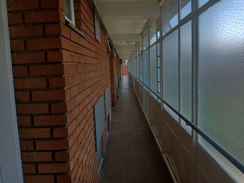 An exterior-facing apartment corridor featuring exposed brickwork, frosted glass paneling, and a metal railing, providing access to residential units.