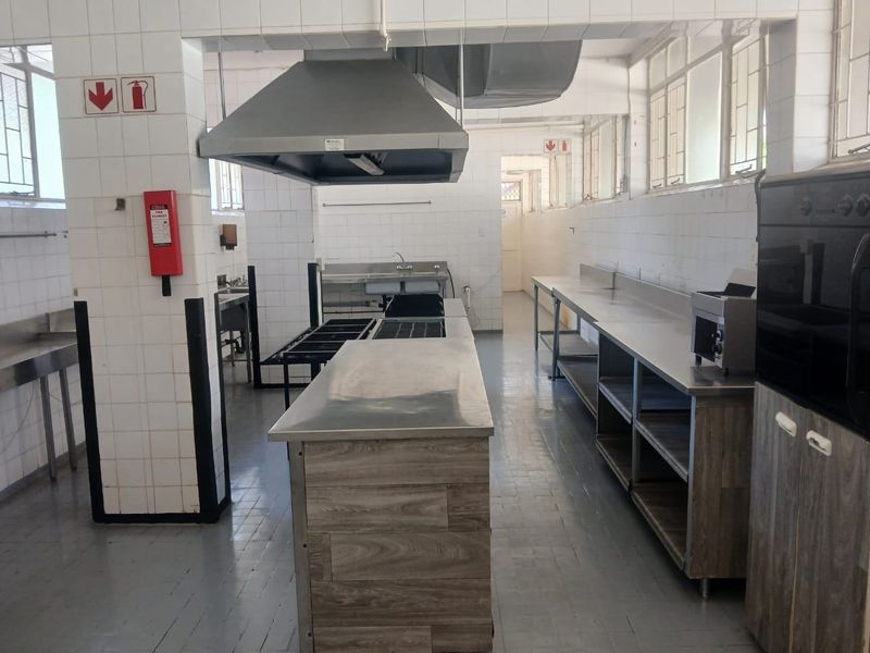 A spacious commercial-style kitchen featuring stainless steel work surfaces, built-in oven, extractor fan, and tiled wall finishes throughout.