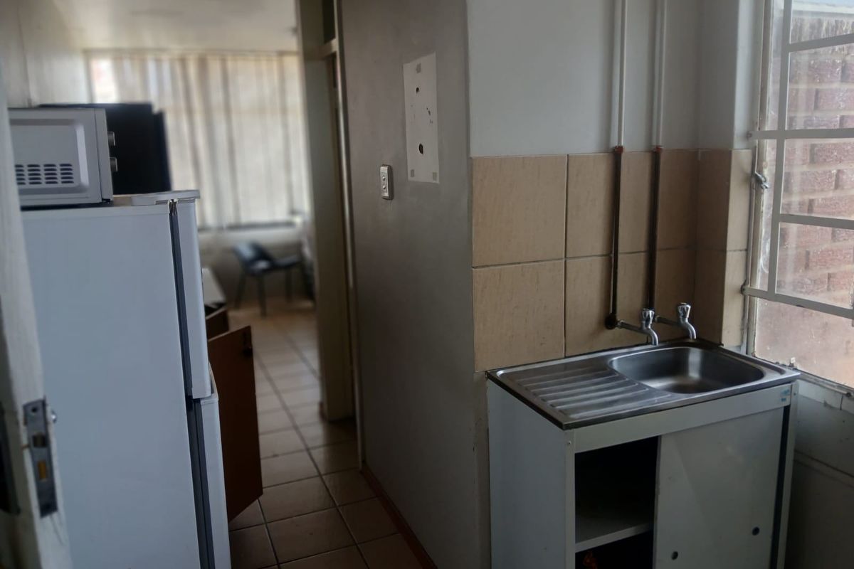 A compact kitchen area featuring a stainless steel sink, tiled splashback, and exposed plumbing, requiring modernization to improve functionality and aesthetic appeal.