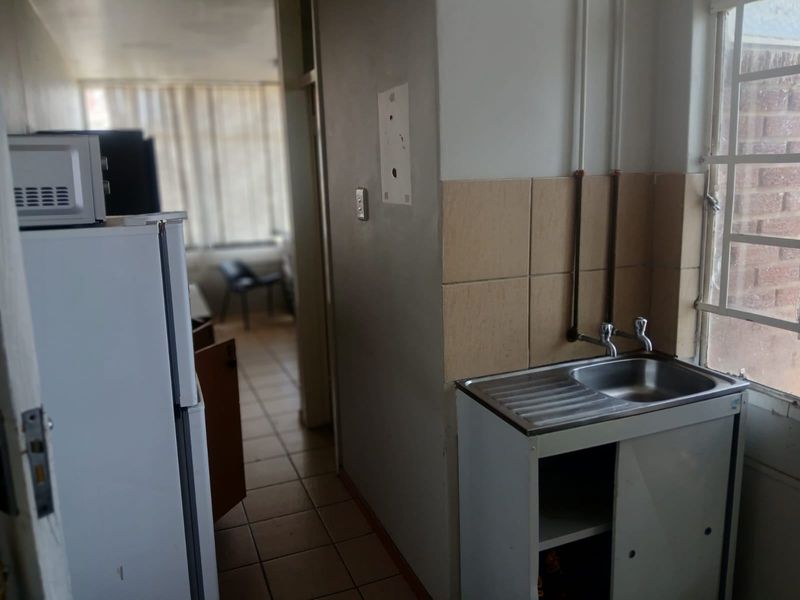 A compact kitchen area featuring a stainless steel sink, tiled splashback, and exposed plumbing, requiring modernization to improve functionality and aesthetic appeal.