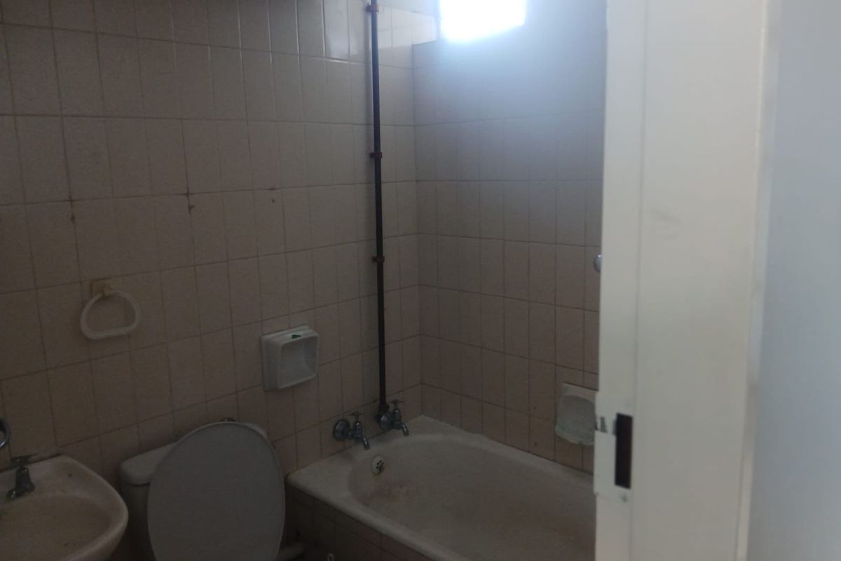 A dated bathroom featuring a bathtub, toilet, and wall-mounted basin with original tiled walls and exposed plumbing, requiring renovation.