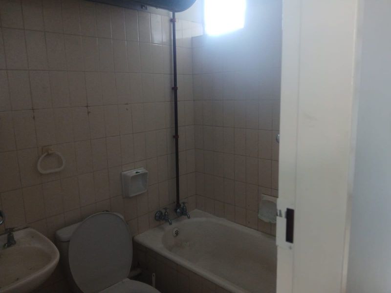 A dated bathroom featuring a bathtub, toilet, and wall-mounted basin with original tiled walls and exposed plumbing, requiring renovation.