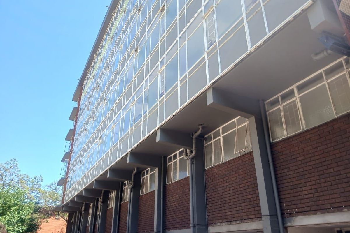A low-angle view of the apartment building exterior, showcasing the brick facade, large glass window panels, and structural concrete elements.