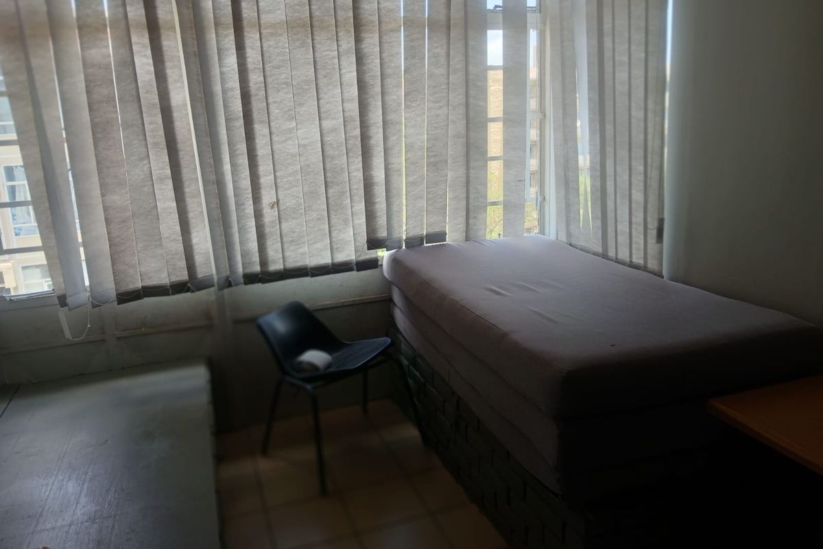 A bedroom featuring tiled flooring and large windows with vertical blinds, offering a functional space that could benefit from cosmetic updates.