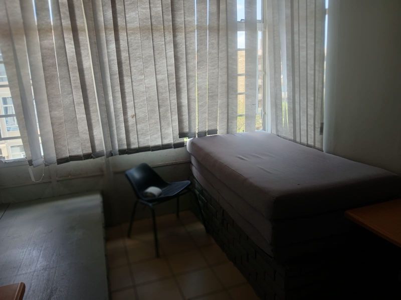 A bedroom featuring tiled flooring and large windows with vertical blinds, offering a functional space that could benefit from cosmetic updates.