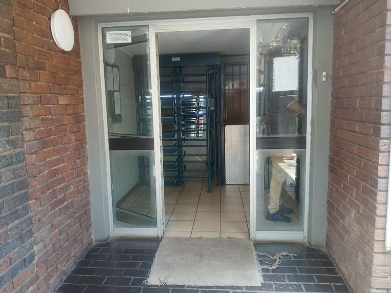 Building entrance featuring a brick facade, glass sliding doors, and a security turnstile system for controlled access.