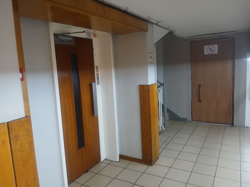 A functional apartment building hallway featuring tiled flooring, an elevator, and access to a staircase.