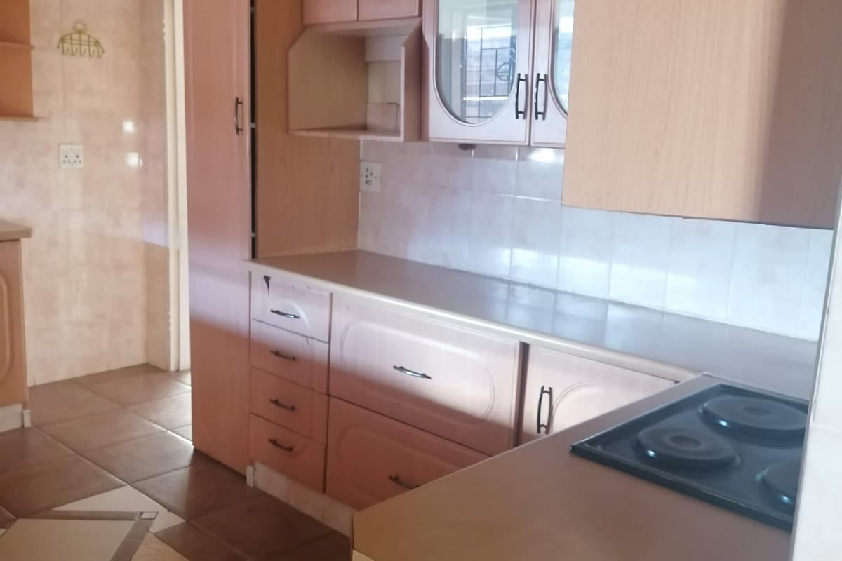 A functional kitchen featuring laminate cabinetry, tiled backsplash, and an integrated electric hob with ceramic floor tiling.