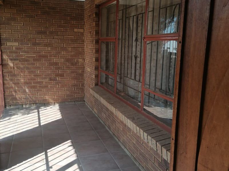 A covered patio area featuring exposed brick walls, tiled flooring, and large windows secured with metal bars.