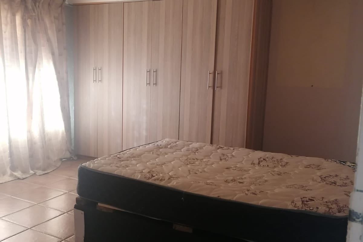 A bedroom featuring built-in cupboards, tiled flooring, and a textured ceiling. The room requires cosmetic updates to improve its overall condition and appeal.
