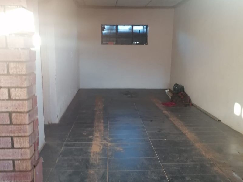An empty, single-car garage space featuring dark tiled flooring and an exposed brick pillar, offering a blank canvas for storage or workshop use.