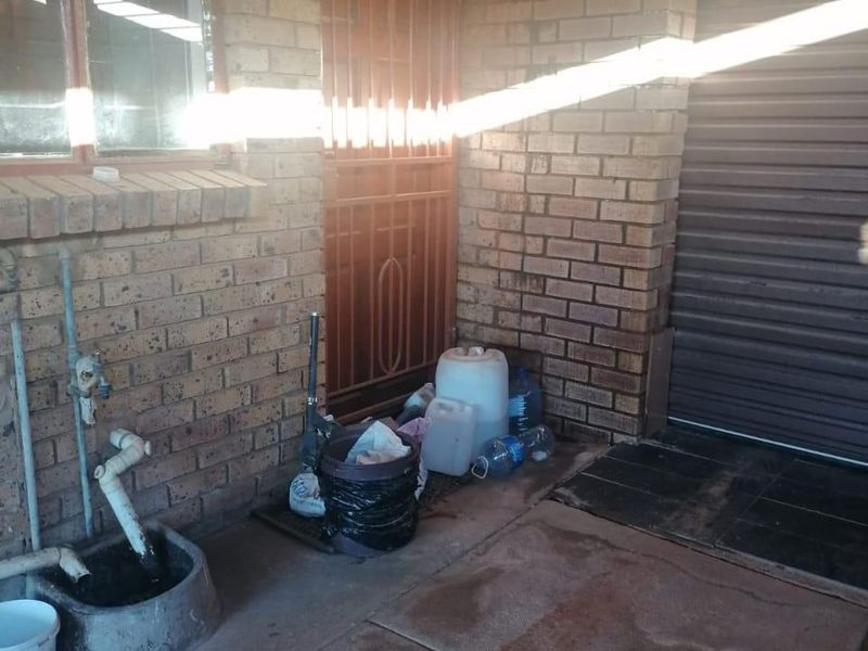 A functional utility area featuring exposed brick walls, a concrete basin with plumbing, and a secure entrance gate adjacent to a garage door.