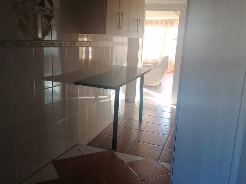 A functional scullery or utility area featuring tiled flooring, wall-mounted cabinetry, and a fixed breakfast bar, leading through to an adjacent living space.