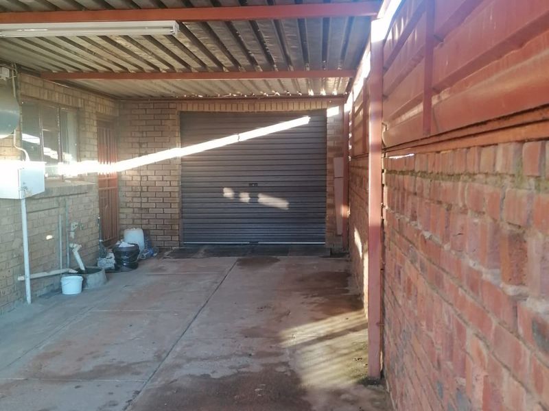 A functional, covered garage area featuring exposed brick walls, a roller shutter door, and a corrugated metal roof structure.