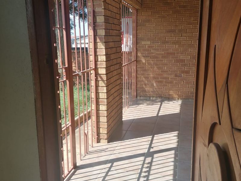 A covered patio area featuring brick pillars, tiled flooring, and a security gate, providing a functional outdoor transition space.