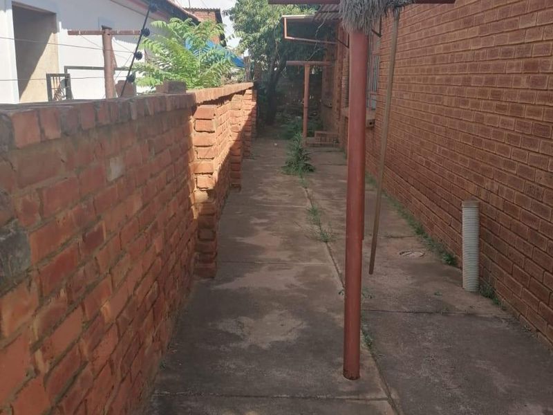 A narrow side passage featuring brick boundary walls, concrete paving, and a fixed metal washing line pole.