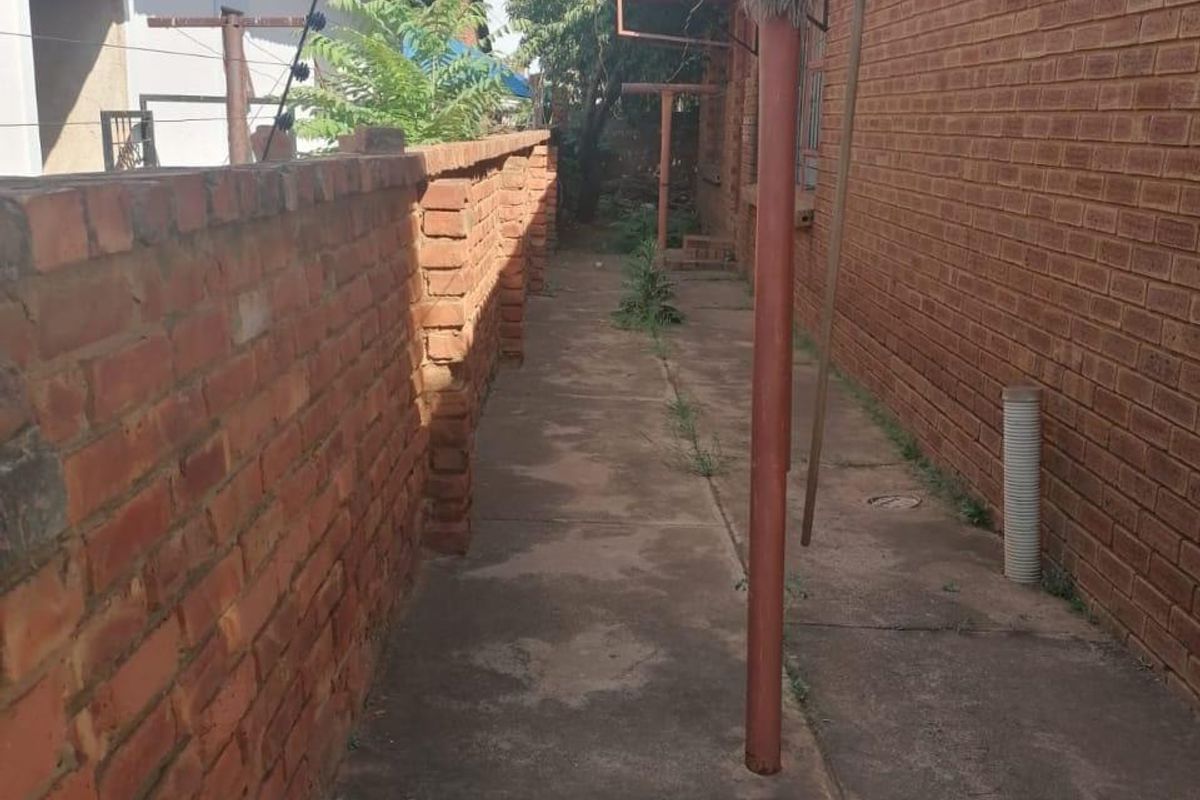 A narrow side passage featuring brick boundary walls, concrete paving, and a fixed metal washing line pole.