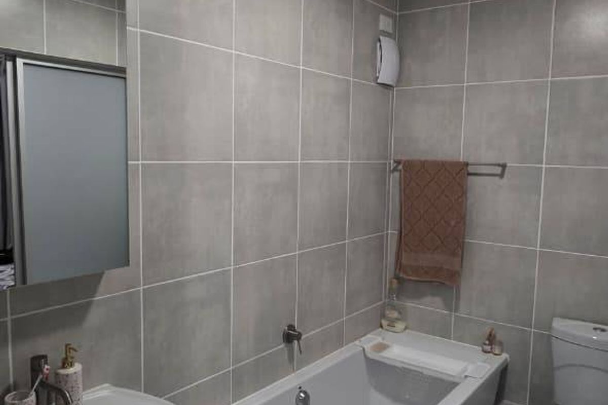 A modern, well-maintained bathroom featuring grey wall tiles, a white bathtub, a pedestal basin, and a standard toilet.