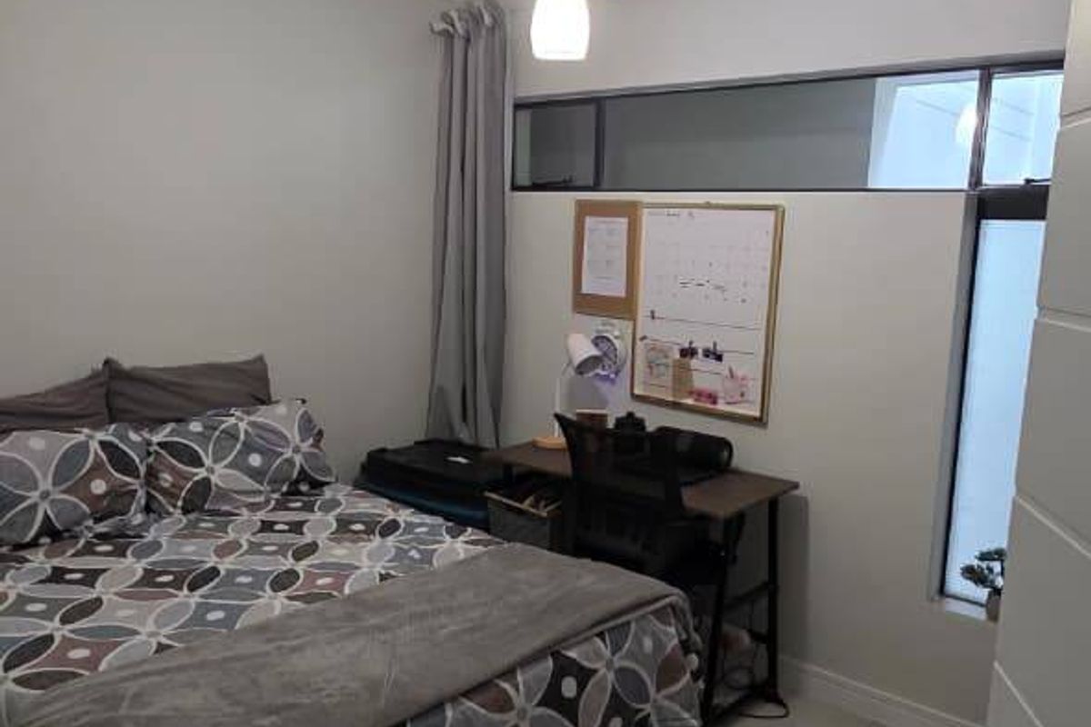 A functional bedroom featuring tiled flooring, a pendant light fixture, and a high-level clerestory window providing natural light.