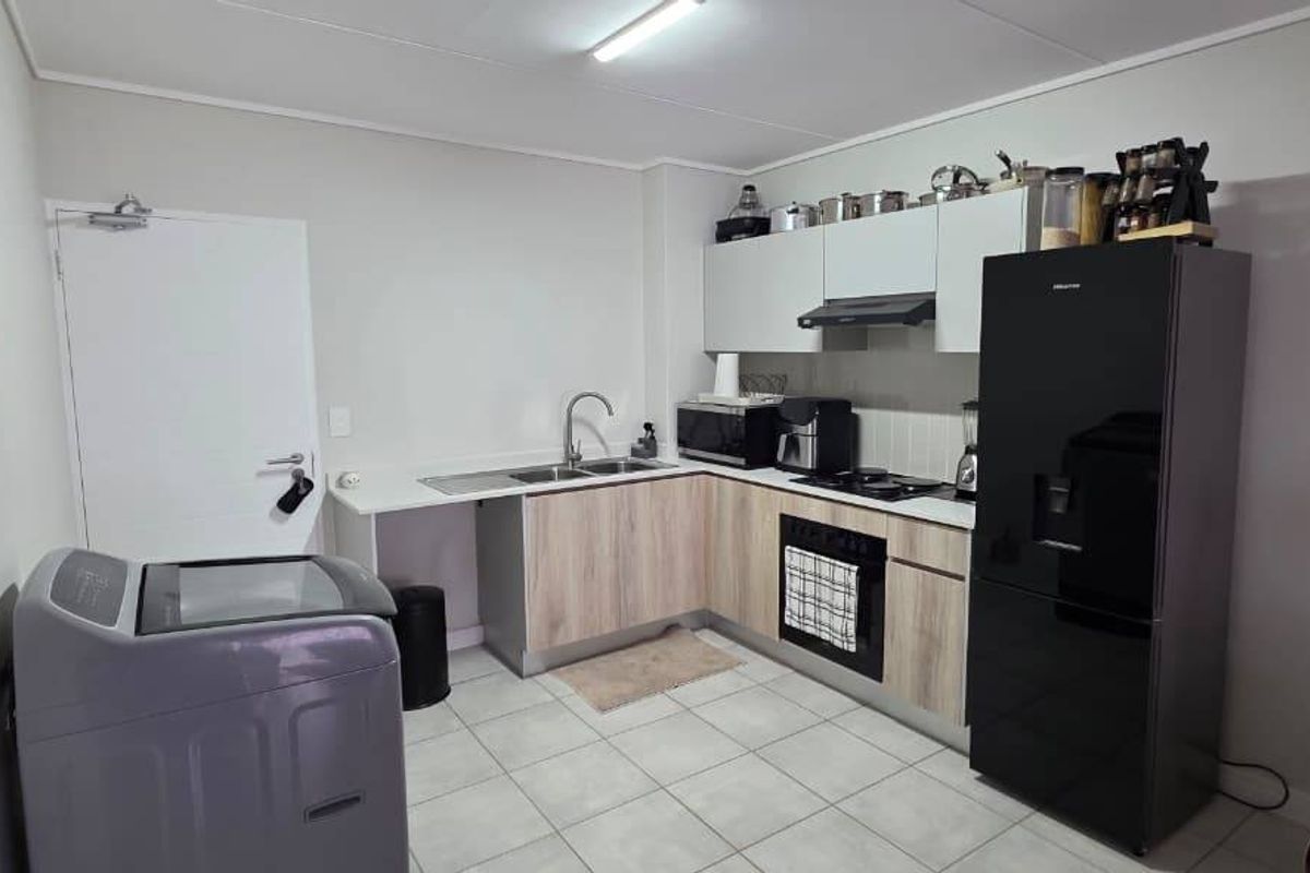 A functional kitchen featuring light wood-look cabinetry, a stainless steel sink, built-in oven, hob, and extractor fan with tiled flooring.