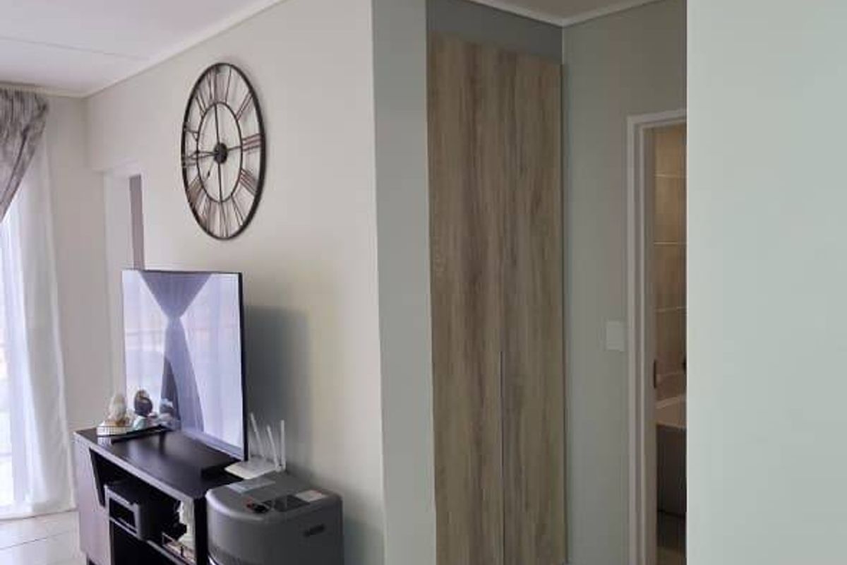 A bright living area featuring neutral tiled flooring, clean wall finishes, and a convenient built-in storage cupboard.