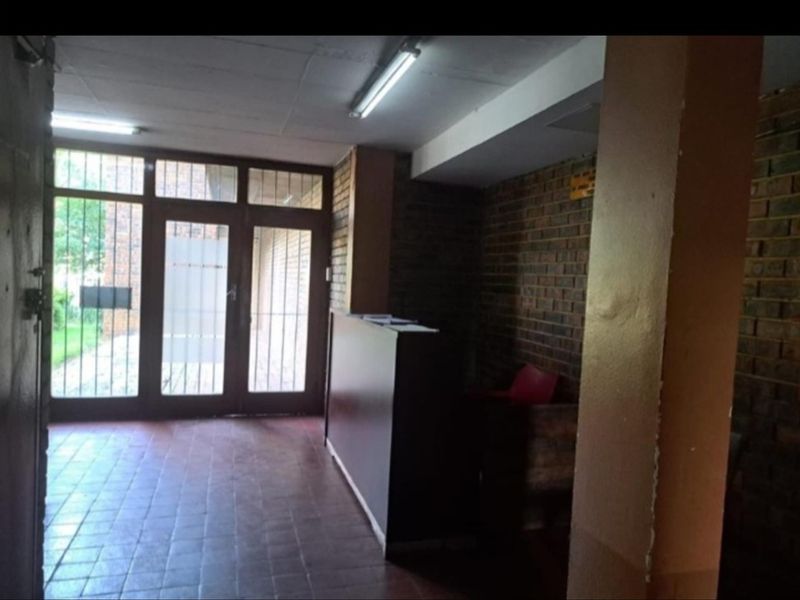 A dated apartment building entrance lobby featuring brick walls, tiled flooring, and secure glass-panelled doors.