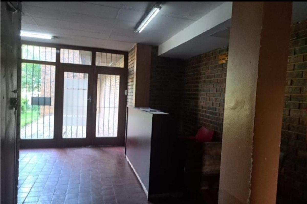 A dated apartment building entrance lobby featuring brick walls, tiled flooring, and secure glass-panelled doors.