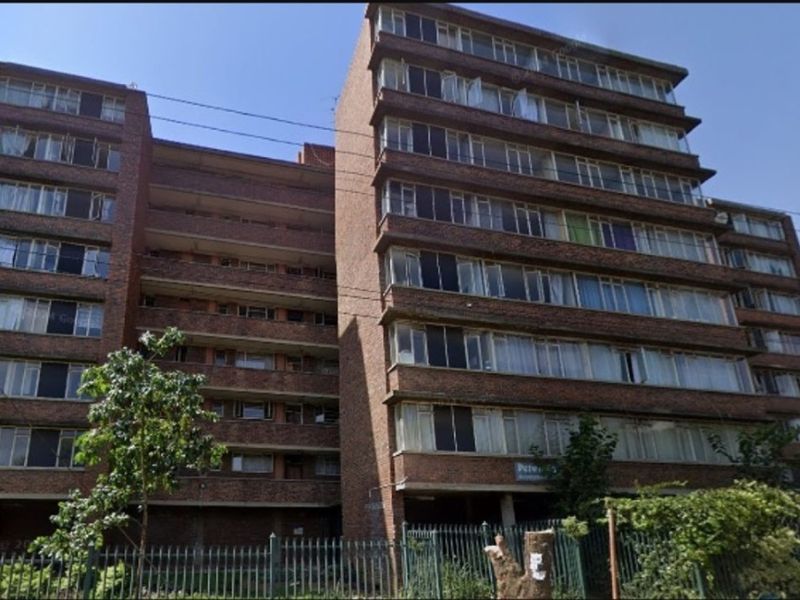 Exterior view of a multi-story brick apartment building featuring traditional casement windows and perimeter security fencing.