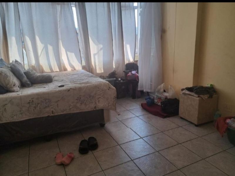 A bedroom featuring tiled flooring and large windows with curtains, providing natural light. The space requires cosmetic updates to improve its overall condition.