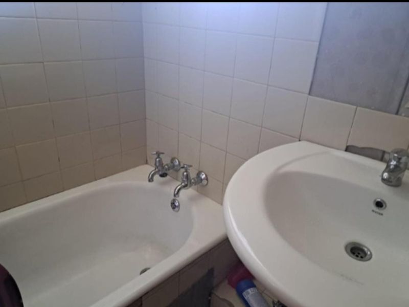 A dated bathroom featuring a bathtub and pedestal basin with visible wall damage and missing tiles, requiring renovation and repair.