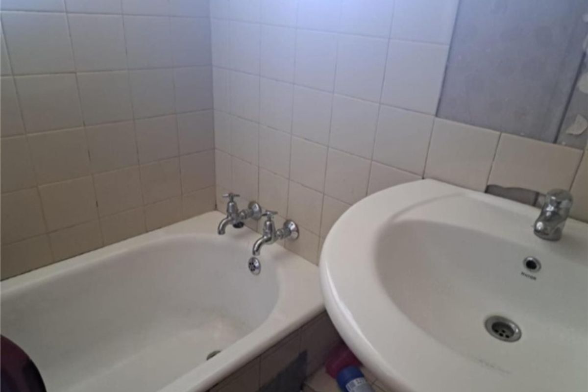 A dated bathroom featuring a bathtub and pedestal basin with visible wall damage and missing tiles, requiring renovation and repair.