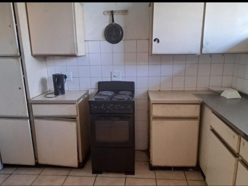 A dated kitchen featuring original cabinetry, a tiled backsplash, and a freestanding electric stove, requiring modernization to improve functionality and aesthetic appeal.