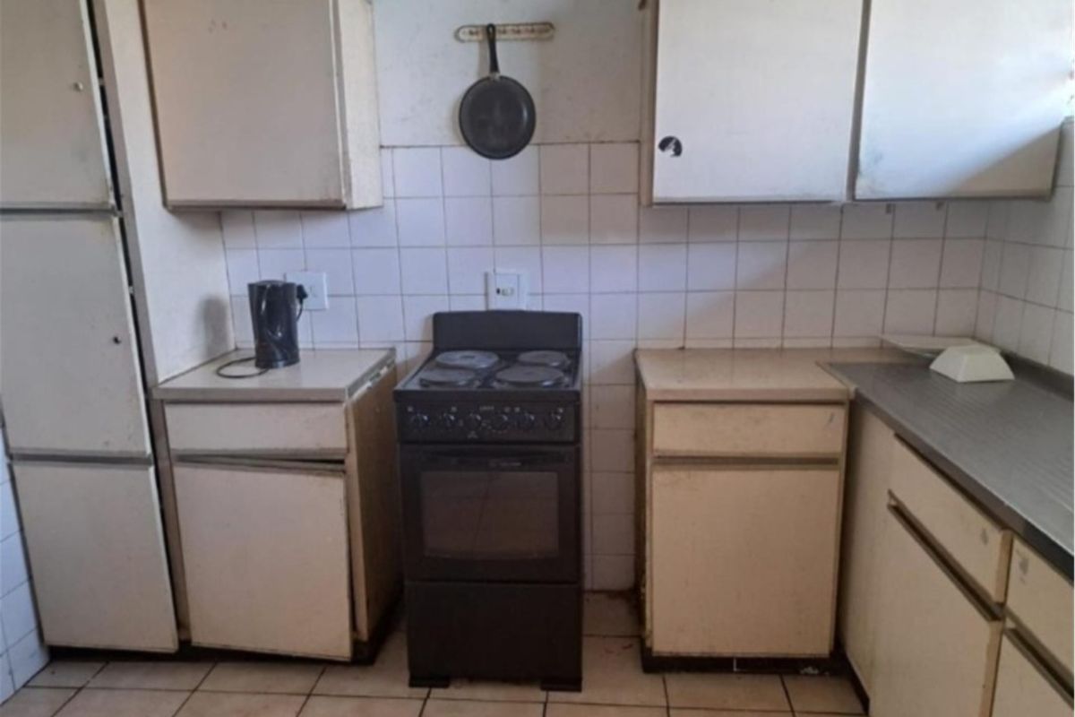 A dated kitchen featuring original cabinetry, a tiled backsplash, and a freestanding electric stove, requiring modernization to improve functionality and aesthetic appeal.