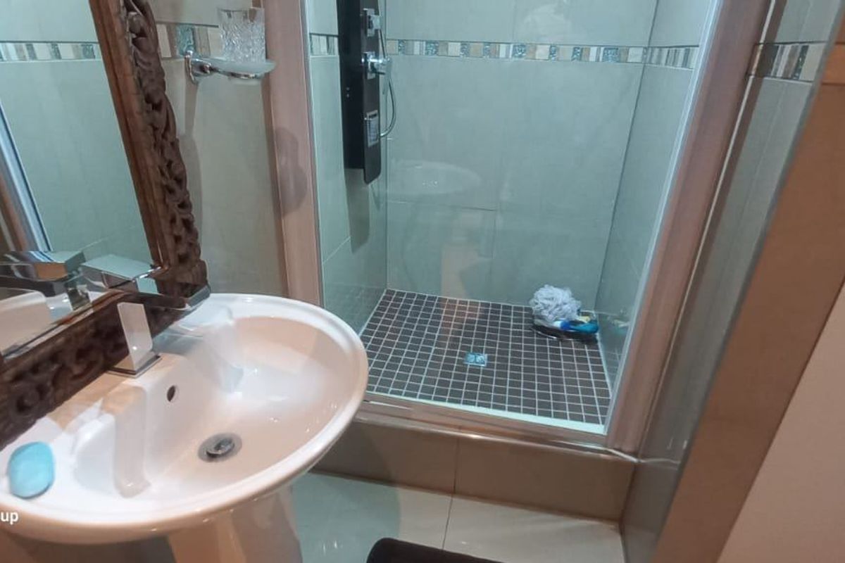 A compact bathroom featuring a pedestal sink, a glass-enclosed shower with mosaic floor tiling, and decorative wall tile accents.