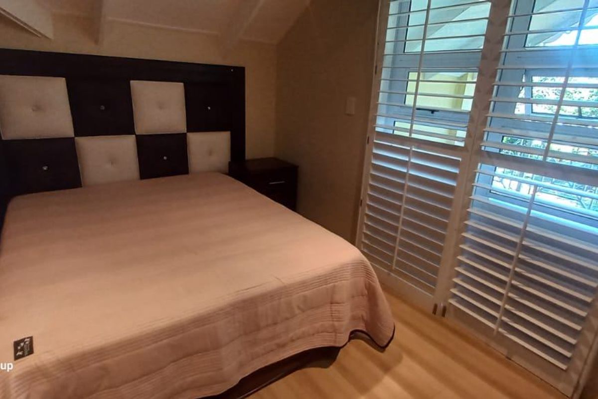 A well-maintained bedroom featuring vaulted ceilings, light wood-look flooring, and white plantation shutters on the windows.