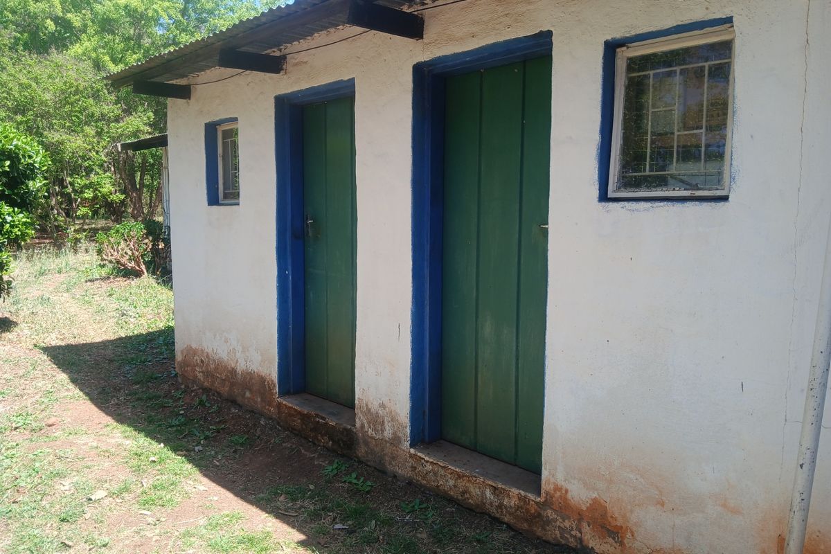 Exterior view of a small outbuilding featuring timber doors, security window bars, and a corrugated metal roof, showing signs of significant weathering.