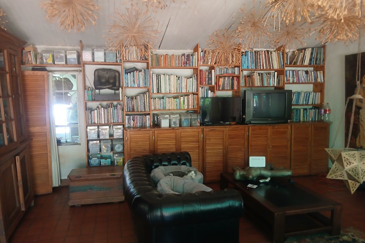 A cozy living room featuring extensive built-in wooden shelving, louvered cabinetry, terracotta flooring, and a vaulted timber ceiling.