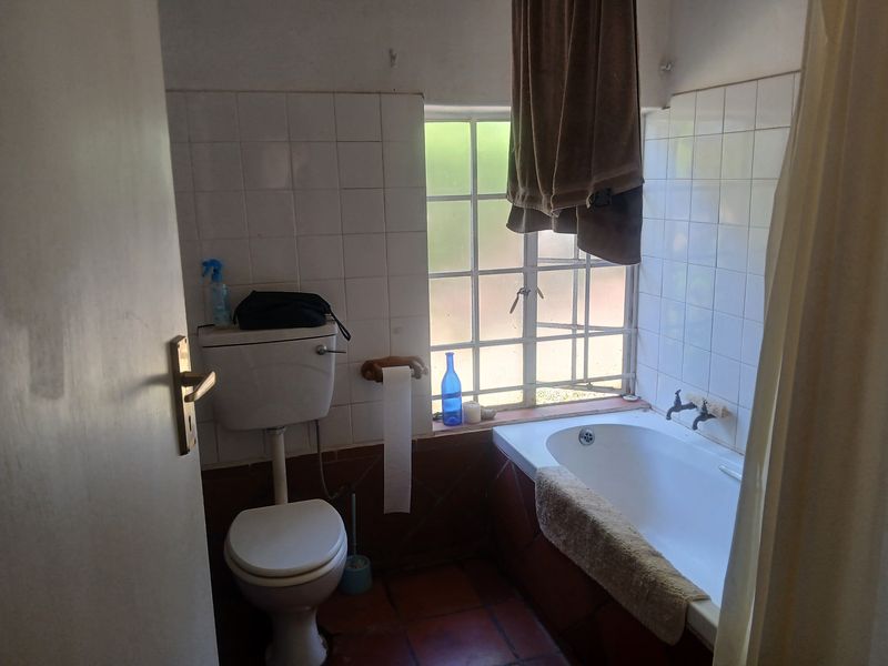 A dated bathroom featuring a built-in bathtub, toilet, and tiled finishes, requiring modernization to improve its overall aesthetic and functionality.