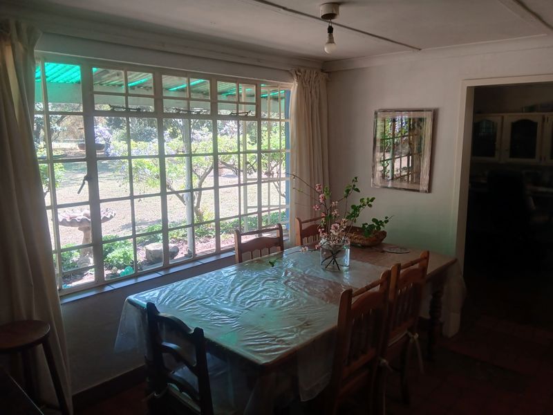 Dining room featuring large grid-pattern windows overlooking the garden, terracotta flooring, and direct access to the kitchen area.