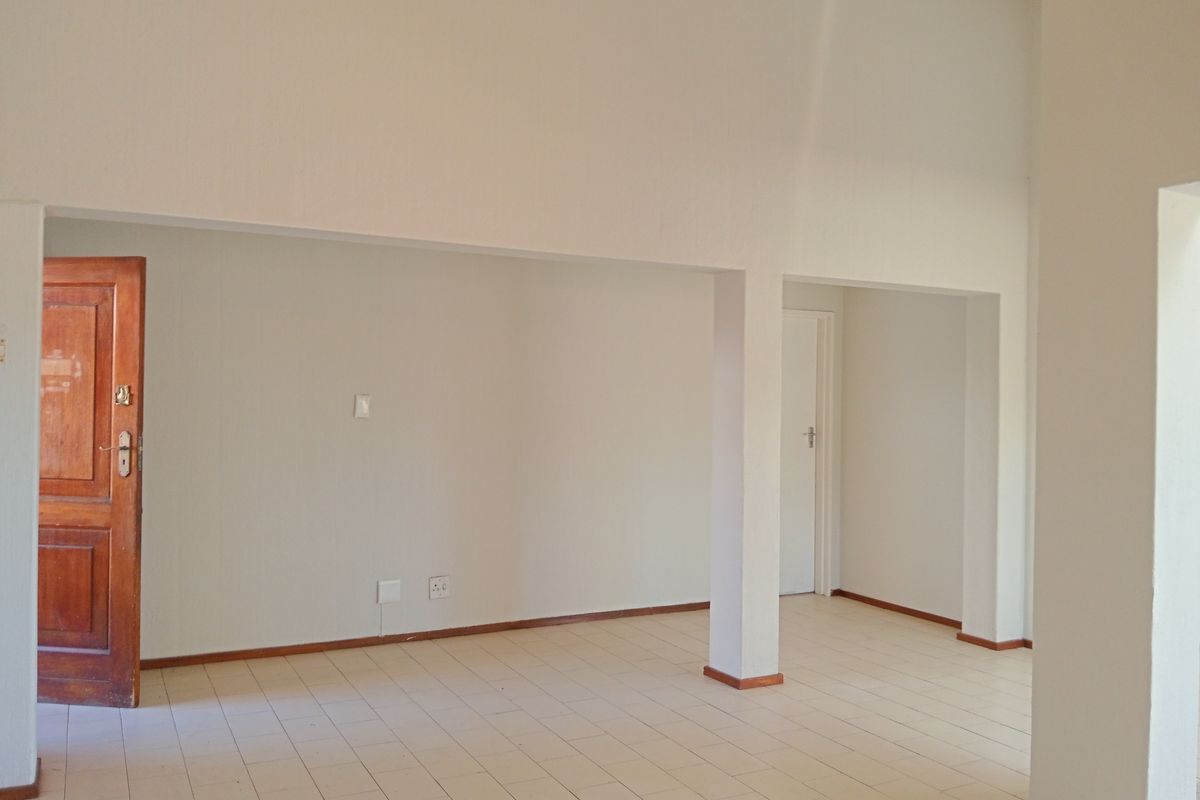 An empty, open-plan living area featuring neutral tiled flooring, structural columns, and a traditional timber door, offering a blank canvas for interior design.