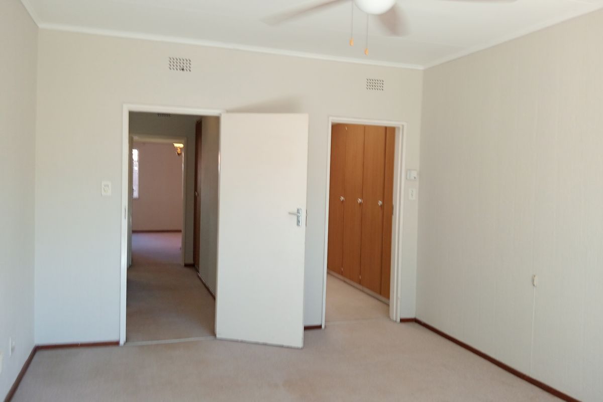 An empty bedroom featuring neutral carpeted flooring, a ceiling fan, and built-in wooden cupboards, offering a clean canvas for personalization.