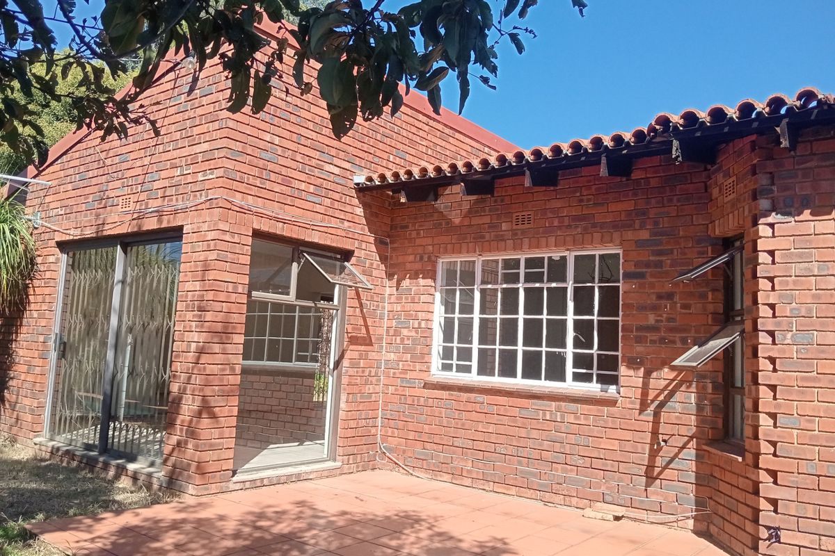 Rear exterior view of a face brick townhouse featuring a tiled patio, sliding glass doors, and traditional terracotta roof tiles with exposed timber rafters.