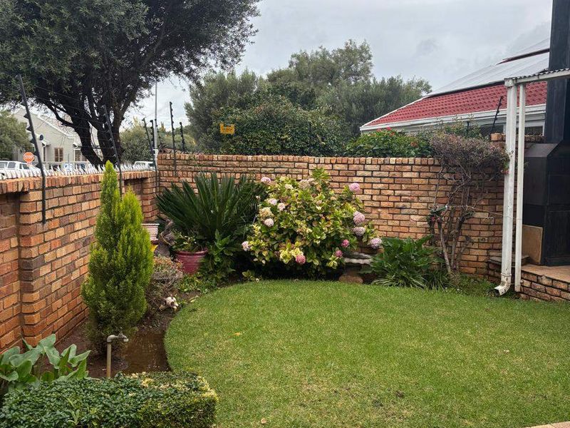 Private rear garden featuring a paved patio, established lawn, brick boundary walls with electric fencing, and a built-in outdoor braai area.