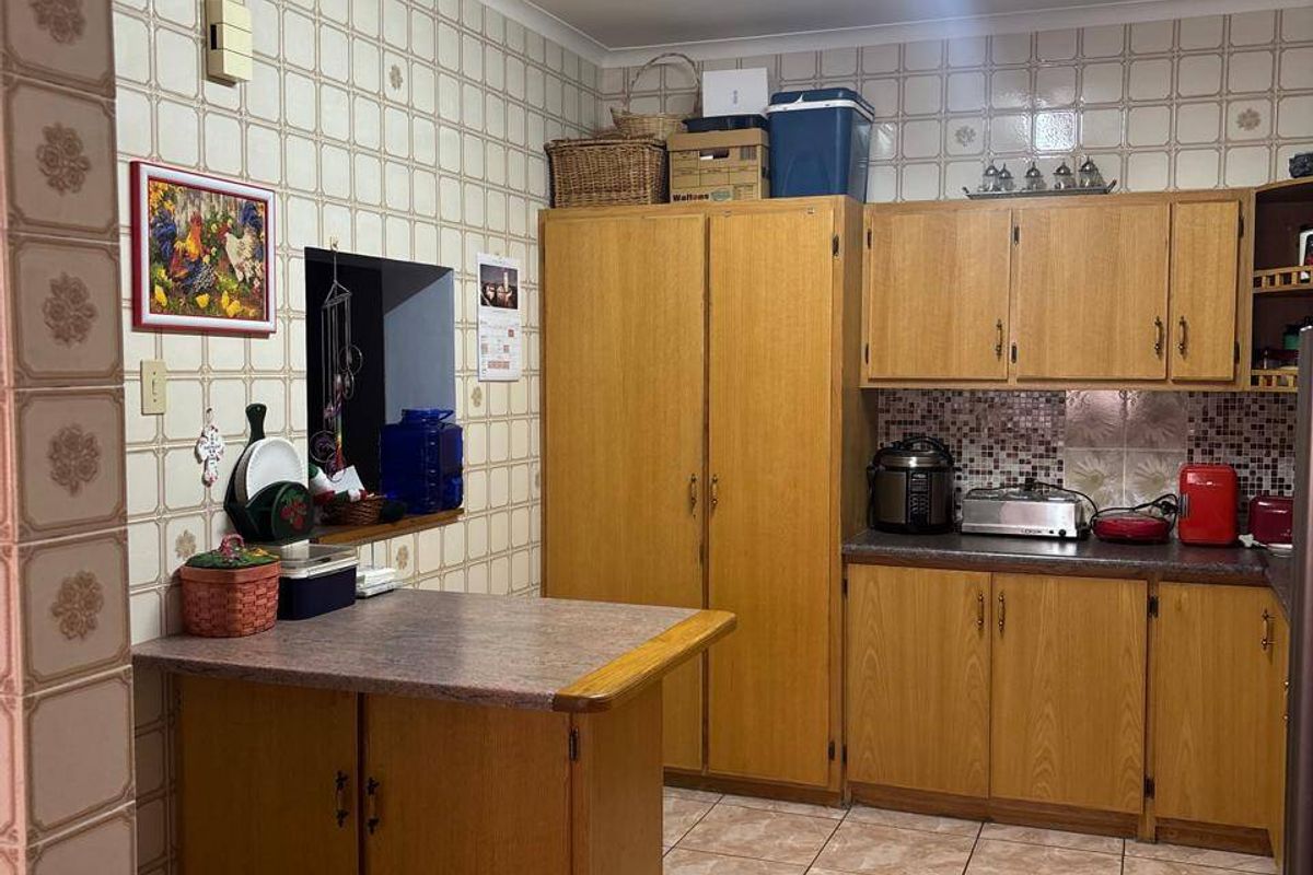 A functional kitchen featuring wood-look laminate cabinetry, tiled walls, and tiled flooring with a convenient pass-through window to the adjacent living area.